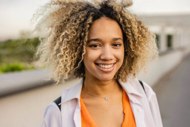 Açık havada gülümseyen güzel kıvırcık saçlı İspanyol kadının portresi.