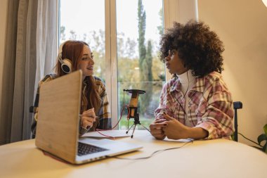 Kadın podcasterler gülüyor ve bir stüdyoda ses yayınında harika vakit geçiriyorlar. Sosyal medya kanalı için internet yayını yapan iki mutlu kadın..