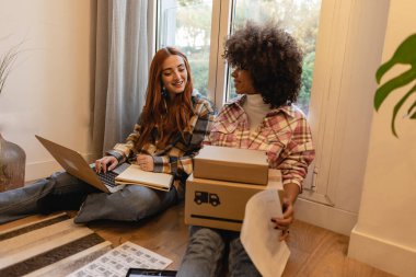 İş yerinde bilgisayarla çalışan küçük bir işletme sahibi. Serbest çalışan iki kadın satıcı ürün siparişini kontrol ediyor. Müşteriye teslimat için mal paketliyorum. Çevrimiçi satış. E-ticaret. Çevrimiçi Alışveriş