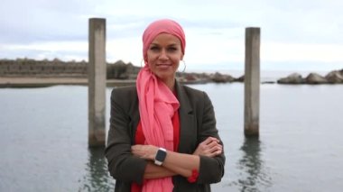 Mutlu olgun bir kadın pembe bir eşarpla gülümsüyor, göğüs kanserine karşı sembol, pozitif kanser savaşçısı konsepti. -