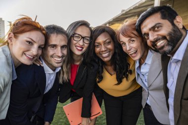 Happy excited diverse business team, mixed race employees of different generations taking selfie in office, holding mobile phone, looking at camera, smiling. Headshot portrait, screen view