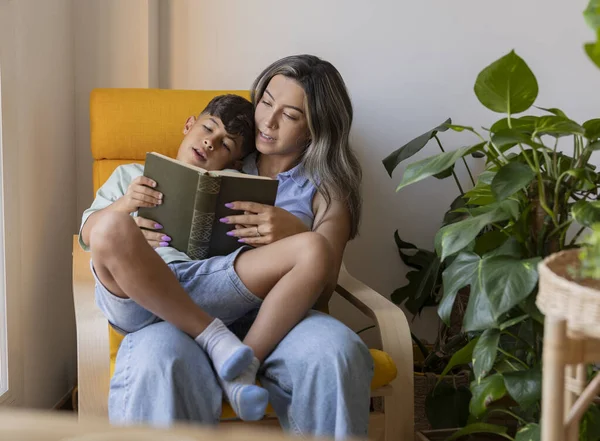 Hispanic mom reading a book with her son at home by the window