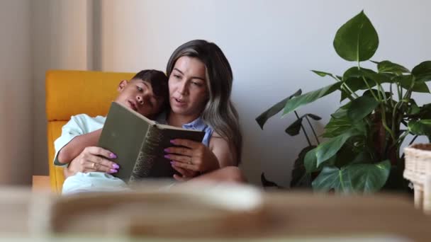 Hispanic Mamma Läser Bok Med Sin Son Hemma Vid Fönstret — Stockvideo