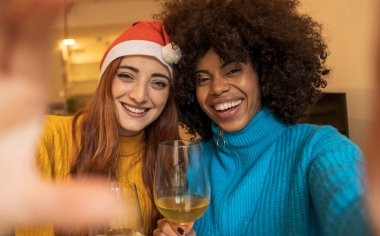 Yılbaşı yemeğinde iki çok kültürlü kadının selfie 'si. Kadeh kaldırma, Noel Baba şapkası takma.