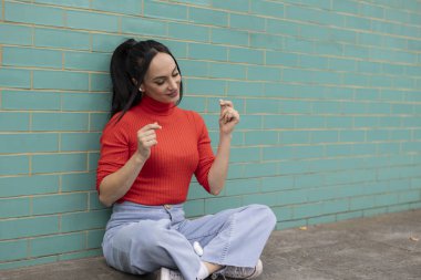 Turkuaz duvara yaslanmış güzel bir kadın kulaklıkla müzik dinliyor.