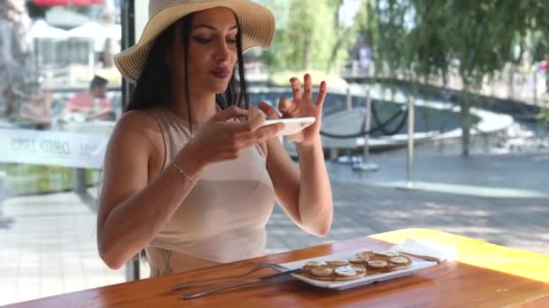팬케이크를 레스토랑에서 모자와 코카서스 여성은 스마트 폰으로 음식에 사진을 만듭니다 — 비디오