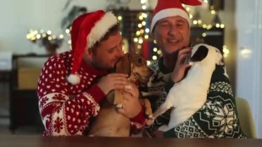 Eşcinsel çiftler Noel 'de Noel Baba şapkalarıyla kameraya bakıp el sallıyor ve öpüşüyorlar. Yavrularıyla birlikteler.