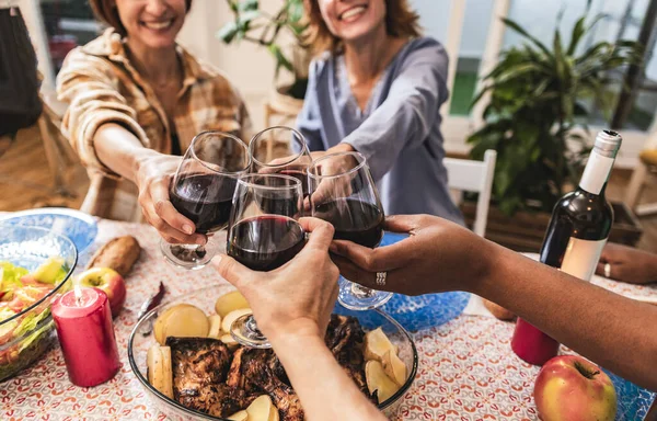 group of generational female friends toasting with wine at dinner - focus on glasses -