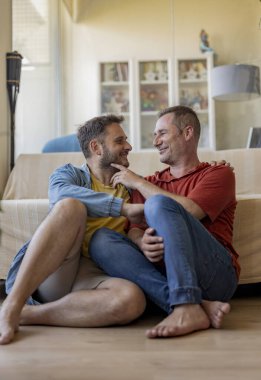 Eşcinsel erkekler evdeki kanepede oturup sevgi gösterirler.