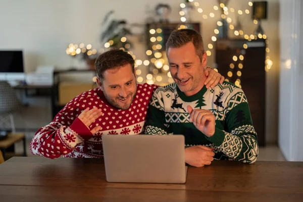 gay men couple celebrate christmas with laptop video call talking with family at home