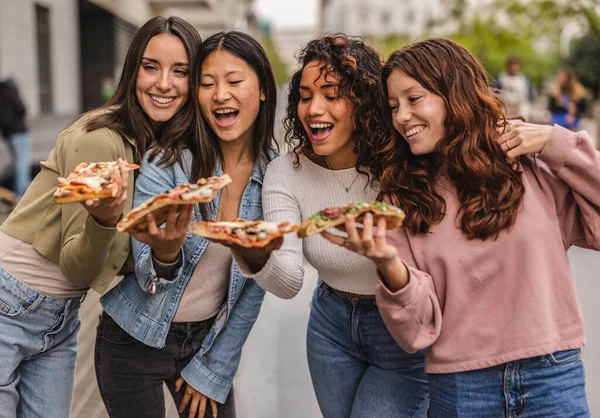 four pretty diverse women eating takeaway pizza in the city