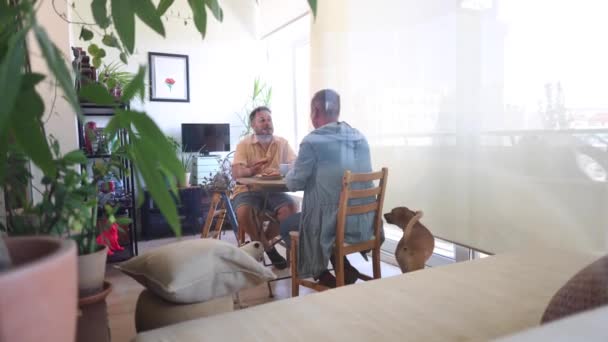 自宅の居心地の良い雰囲気の中で ゲイのカップルは共有の朝食を楽しんで 犬と一日のトーンを設定する貴重な瞬間を作成しました — ストック動画
