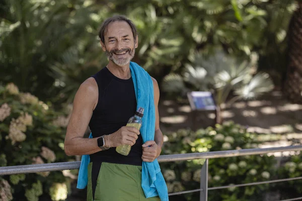 Senior athlete man resting towel and energy drink, smiling about finishing his workout