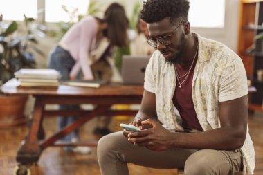 Ofiste çalışan meslektaşlarında akıllı telefon kullanan Afrikalı bir adamın portresi.
