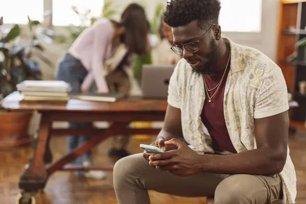 Ofiste çalışan meslektaşlarında akıllı telefon kullanan Afrikalı bir adamın portresi.