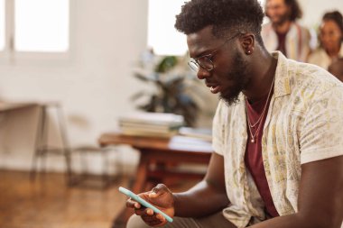 Ofiste akıllı telefon kullanan Afrikalı bir adam. Arka planda iş arkadaşları, cep telefonu kullanan genç bir öğrenci.