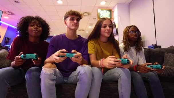 一群年轻的多种族青少年在沙发上和控制器玩电子游戏 — 图库视频影像