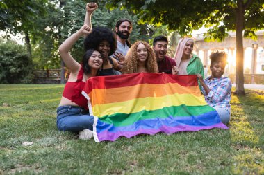 Eşcinsel gurur gününde gökkuşağı bayrağıyla gösteri yapan çeşitli etnik çeşitliliğe sahip genç insanlar..