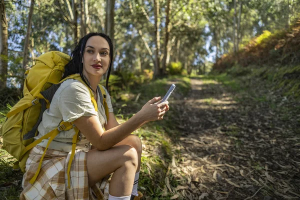 pretty female hiker resting in the forest looking at her smart phone