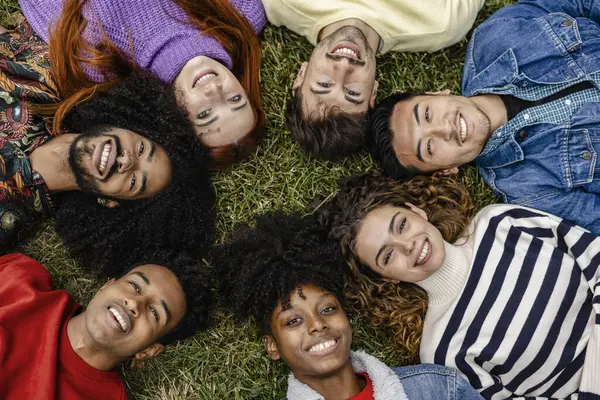 Close-up of a multiracial group of young people, a diverse group of young adults representing unity, friendship, teamwork and community lying on the grass in a circle
