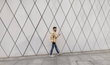 Profilde gülümseyen Latin bir adam şehir caddesinde yürürken telefonuna bakıyor.