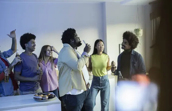 Group of happy multiethnic friends singing karaoke during a party in the apartment, toasting and cheering