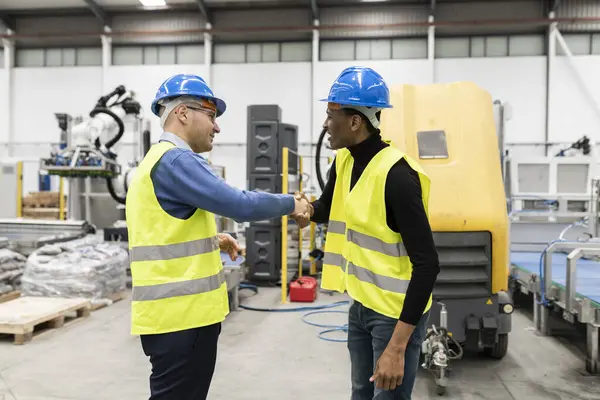 Chief engineer and project manager wear safety vest and helmet, greet and talk to new worker and program machines to increase productivity.