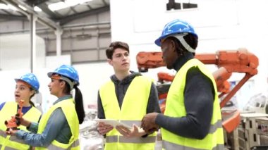 Modern fabrika: Erkek mühendis proje yöneticisi güvenlik önlüğü, kask giyiyor, atölyede çalışıyor, konuşuyor, dijital tablet kullanıyor ve CNC makine montaj hattını izliyor