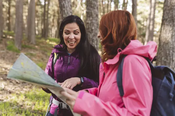 adult female hiker friends having a fun time while looking at the trail route on the map