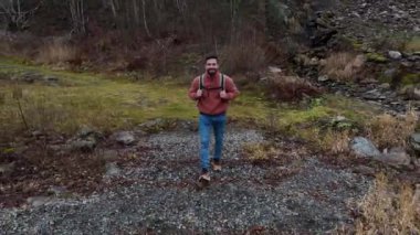 tourist man with jacket and backpack walking in front of the fjord. Back view of a hiker alone by the sea of the coast between mountains