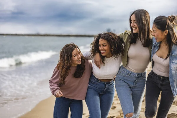 group of multicultural friends standing in a row looking at their friend laughing on the beach
