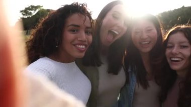 Genç çok ırklı insanlar akıllı telefonlarıyla selfie çekiyor ve açık havada eğleniyorlar..