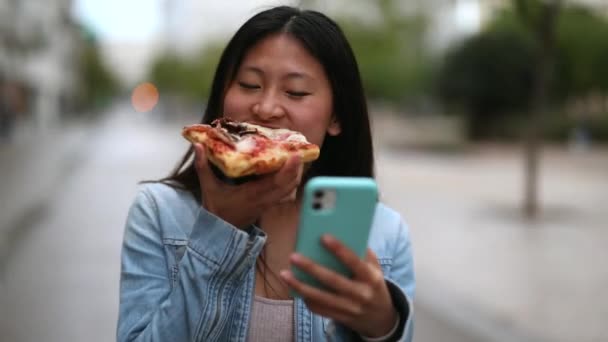 Азіатська Жінка Їсть Піцу Ходить Дивлячись Свій Смартфон — стокове відео