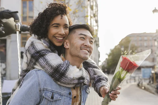 girlfriend carried on her boyfriend\'s shoulders while carrying a bouquet of roses at sunset on their Valentine\'s date