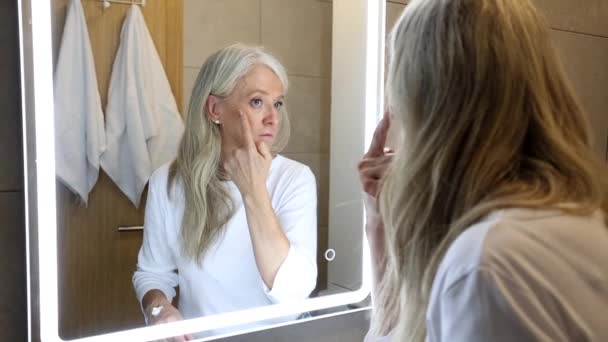 Ανώτερη Γυναίκα Στο Μπάνιο Κοιτάζοντας Στον Καθρέφτη Φροντίζει Πρόσωπό Της — Αρχείο Βίντεο