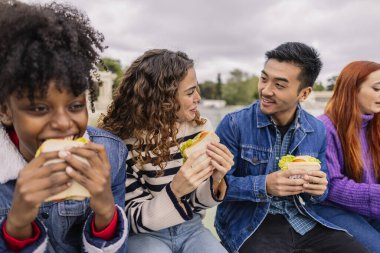 Çok ırklı arkadaşlar üniversite tatillerinde atıştırmalık sandviç yiyorlar.