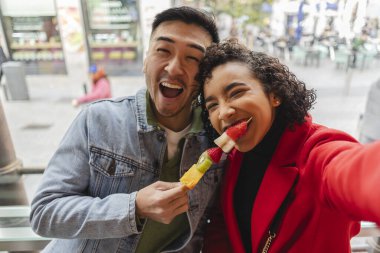 Çok ırklı bir çiftin tatilde kameraya baktığı komik bir selfie.
