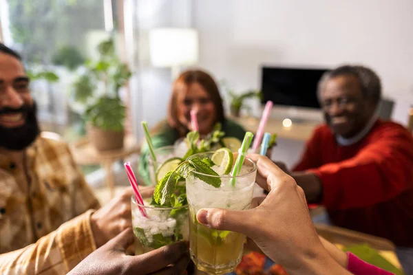 Group of multiethnic friends drinking and toasting with glasses of mojito in their living room- Young people food and drink lifestyle concept