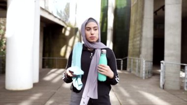 Spor kıyafetleri giyen müslüman kadın dinleniyor su içiyor ve havluyla kuruyor.