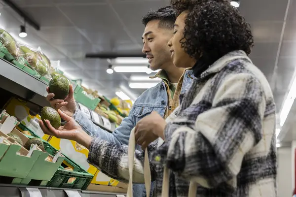 Happy couple buying food in supermarket, choosing avocados to prepare healthy food at home