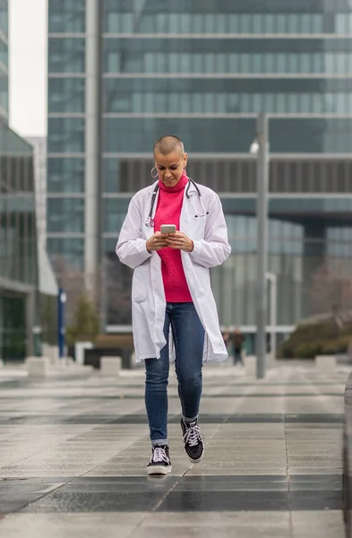 female doctor in lab coat walks looking at her phone