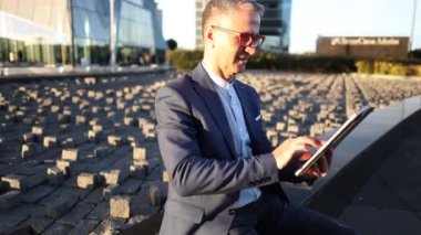 Gün batımında finans alanında dijital tablet kullanan gri saçlı yetişkin iş adamı