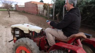 Olgun bir adam gün batımında traktör sürüyor.