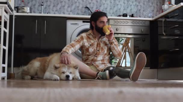 ビオニックの脚を持った男 彼のアパートで 犬と一緒にキッチンに座って コーヒーを飲んで — ストック動画