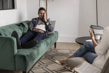 Bir adam terapi seansında kanepede yatarken üzgün görünüyor.