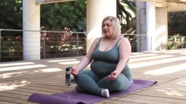 Kavisli kadın dışarıda yoga yapıyor.