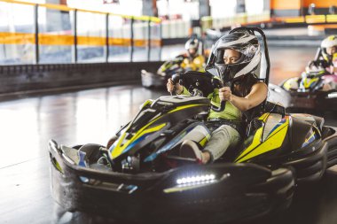 Miğferli ve yarış eldivenli genç bir kadın kapalı bir go-kart yarışında yarışıyor..