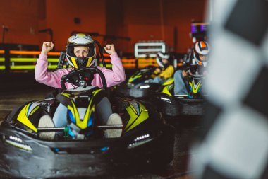 Neşeli genç bir kadın, bir karting yarışından sonra yumruklarını kaldırıyor..