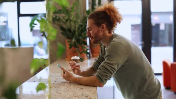 Kıvırcık Saçlı Genç Bir Adam Kahve Molası Sırasında Akıllı Telefonunu — Stok video