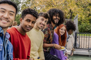 Suyun kenarında oturan farklı arkadaşlar, şehirde birlikte yemek yiyorlar..